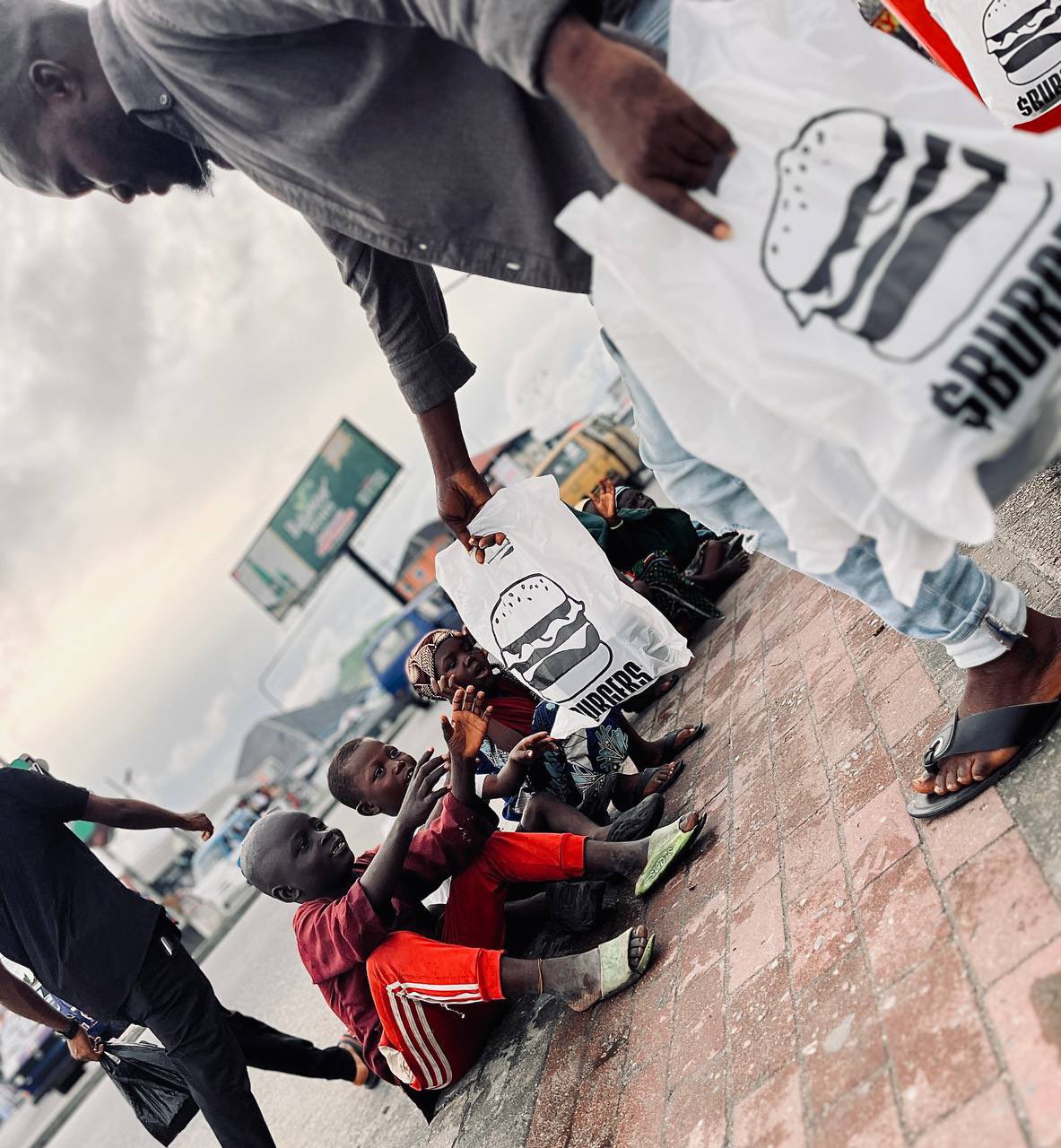 A $BURGERS meal bag being handed to a child on the street